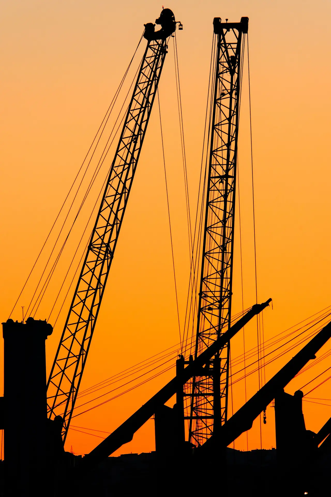 Construction cranes silhouetted against a golden sunset